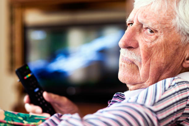 istock Grumpy old man turns from TV frowning, holding remote control 660621680