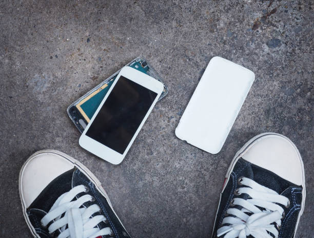 istock Broken smart phone after being dropped on concrete grunge floor between owner's sneaker shoes 660622100