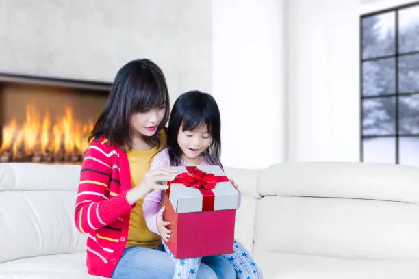 Portrait of beautiful mother and cute child opening gift box together while sitting on the sofa