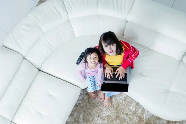 Top view of beautiful mother using a laptop while sitting on the couch with her daughter
