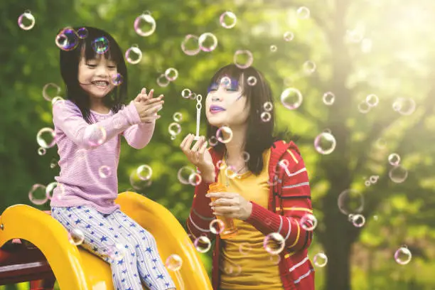 Portrait of beautiful mother blowing soap bubbles while playing with her daughter in the playground