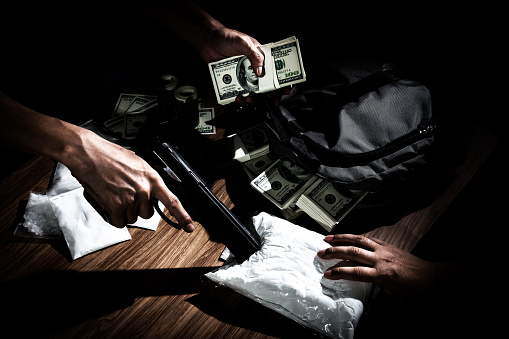 El traficante de drogas usa el arma para empujar el sobre de la mesa al comprador photo