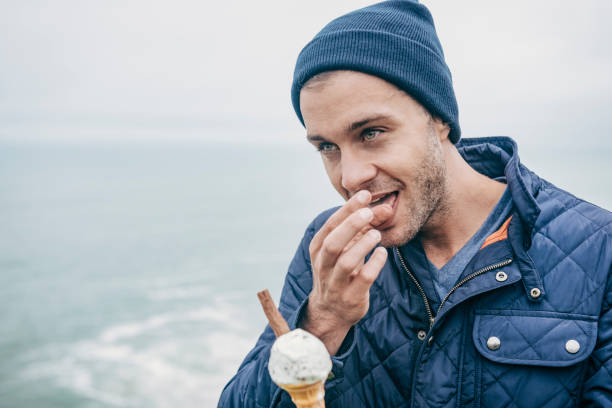 istock Man licking his fingers, eating an ice cream, Cornwall, Autumn. 660681374