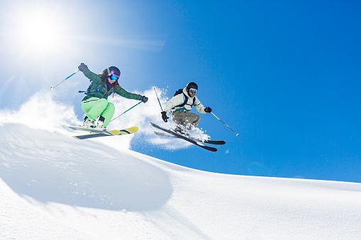 Young woman and man skiing and jumping in powder snow