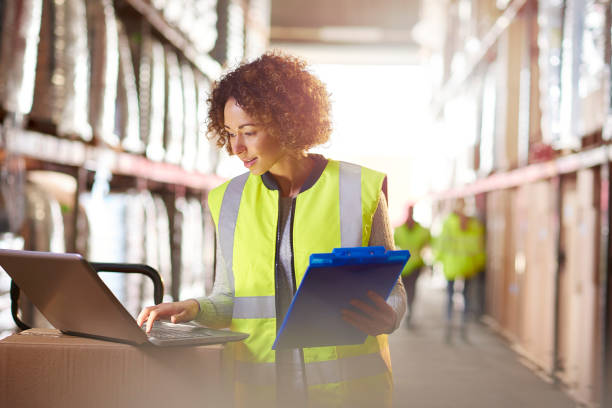 warehouse stock check a female warehouse manager looks at her stock on a laptop checking her delivery sheet in the warehouse . distribution warehouse stock pictures, royalty-free photos & images