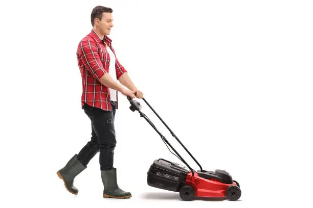 Full length profile shot of a gardener mowing with a lawnmower isolated on white background