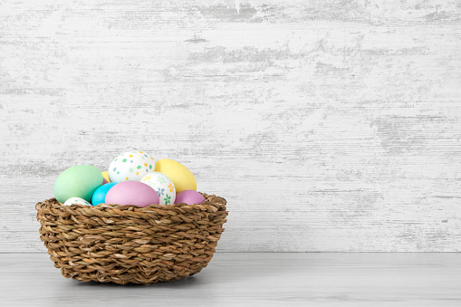 Easter eggs painted in pastel colors in a basket on white wooden background.