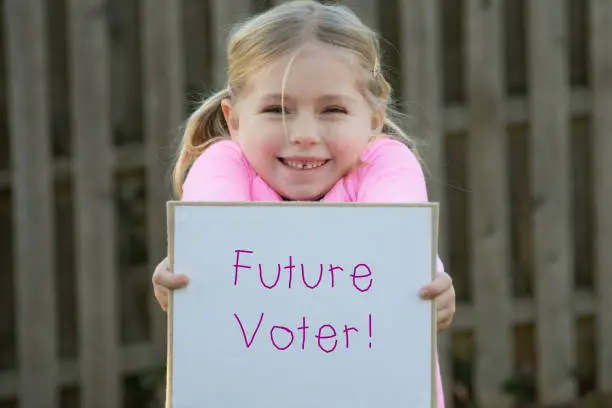 young girl child wearing pink for women's rights and holding sign that says future voter