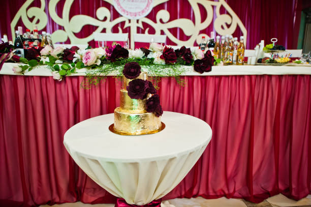 Golden wedding cake with delicious flowers at small table.