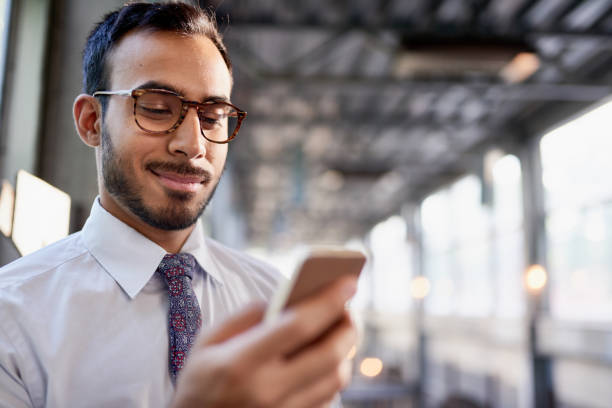Indian businessman smiling confidently and surfing the net on a smartphone Portrait of a confident, happy business entrepreneur wearing fashionable tie and eyewear on his way to his next consultant meeting on the train platform necktie photos stock pictures, royalty-free photos & images