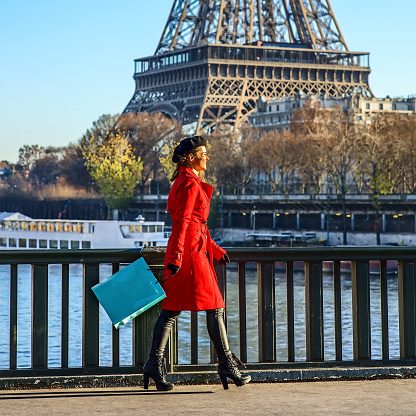 Bright in Paris. Full length portrait of happy elegant woman in red trench coat on embankment near Eiffel tower in Paris, France walking