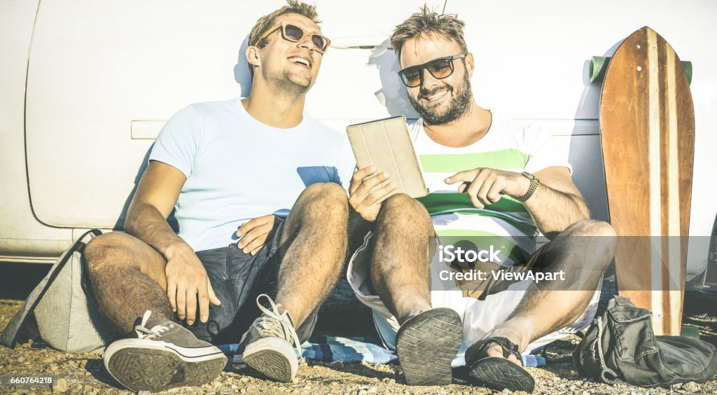 Hipster best friends having fun with tablet at car trip moment - Modern friendship and technology concept with always connected young people at alternative travel experience - Retro contrast filter Male Friendship Stock Photo