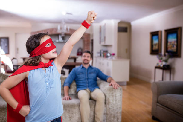 istock Daughter pretending to be a superhero while father sitting on sofa 660778698