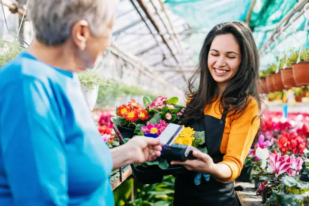 Senior woman buying flowers and making a contactless credit card payment in the nursery