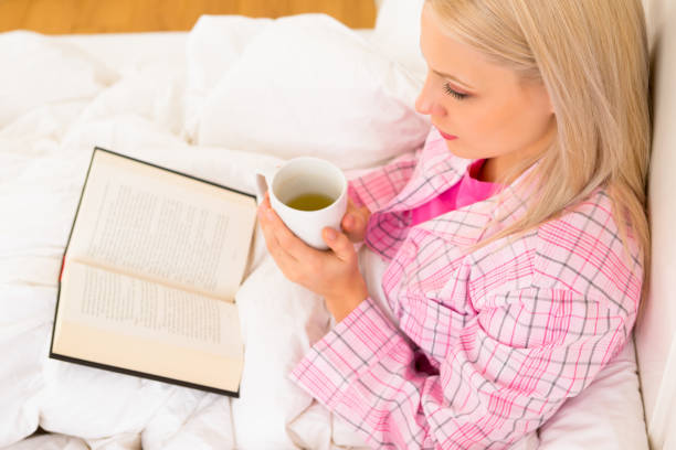 istock High angle view of woman holding mug and reading book 660802306
