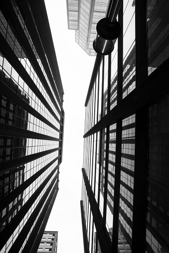 A black and white image of the view looking up the walls of urban glass towers.