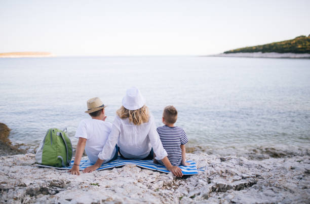 Enjoy sea at sunset A photo of a three member family. They are sitting by the beach and enjoy the end of the summer day family beach vacations travel stock pictures, royalty-free photos & images