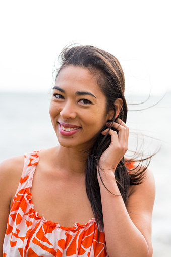 Lifestyle portrait of an attractive Hawaiian woman wearing a flower dress at Kahana Bay on Oahu Hawaii.