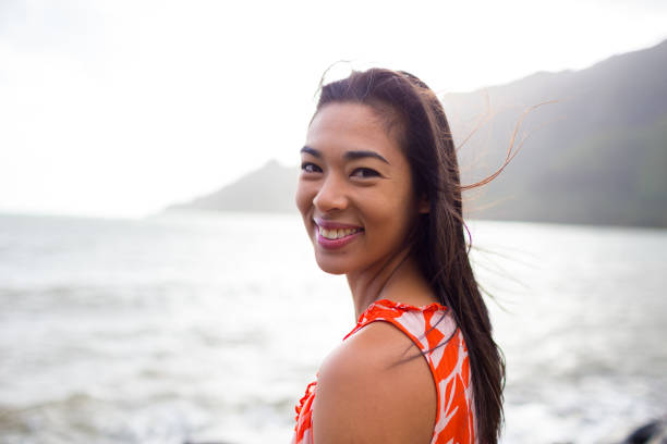 Lifestyle portrait of an attractive Hawaiian woman wearing a flower dress at Kahana Bay on Oahu Hawaii.