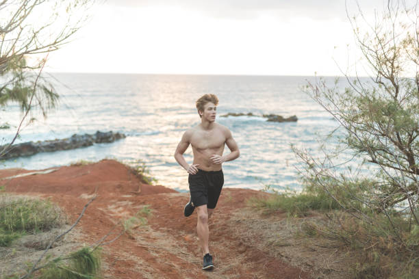 il giovane in forma corre a torso a torso libero lungo la spiaggia delle hawaii - men beach running shirtless foto e immagini stock