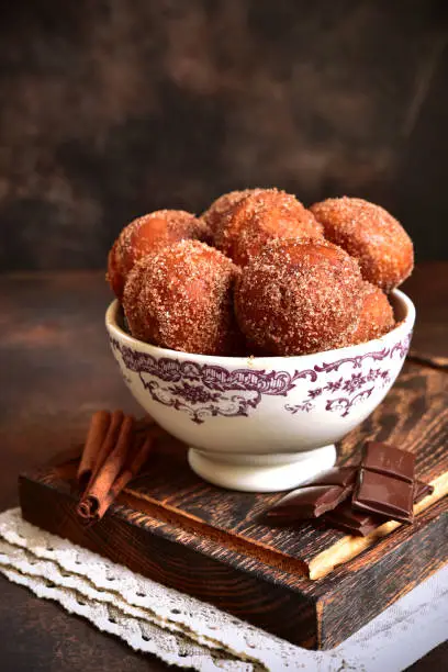 Stack of homemade fried vanilla donut with cinnamon,sugar and chocolate sauce in a vintage bowl on a dark slate background.