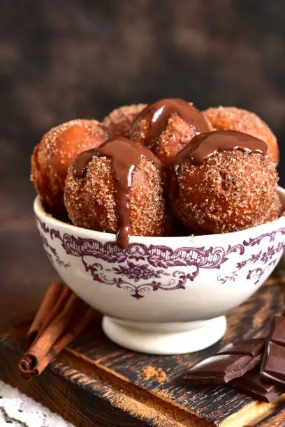 Stack of homemade fried vanilla donut with cinnamon,sugar and chocolate sauce in a vintage bowl on a dark slate background.