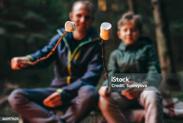 Father And Son Prepear To Bake Marshmallow Candies On Campfire Stock Photo - Download Image Now