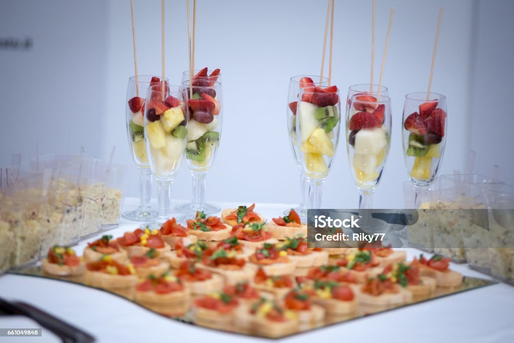A plate full of little snack anda glasses of fruit A plate full of littel snack with bread, tomatos and corn. And glasse ful of fruit strawberry, pineapple, apple and kiwi Appetizer Stock Photo
