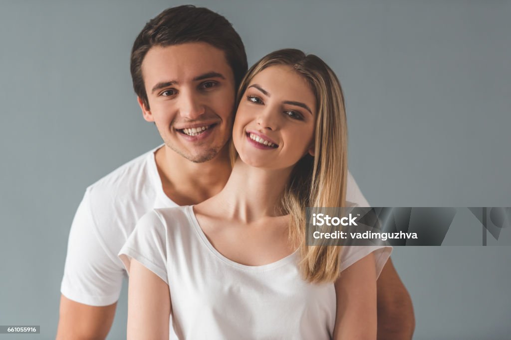 Beautiful young couple Beautiful young couple is hugging, looking at camera and smiling, on gray background Adult Stock Photo