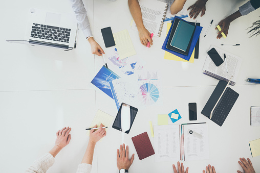 Overhead view of business meeting with hands, planners, and computers