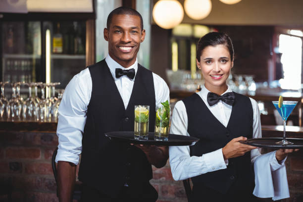 Waiter and waitress holding a serving tray with glass of cocktail Portrait of waiter and waitress holding a serving tray with glass of cocktail waitress stock pictures, royalty-free photos & images