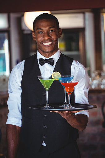 Portrait of smiling bartender holding serving tray with cocktail glasses