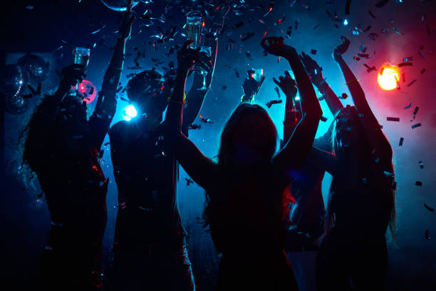Nightclub party with confetti Silhouette of young people with raised flutes having fun and clubbing dance floor stock pictures, royalty-free photos & images