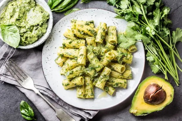 Vegetarian green pasta with avocado and herbs sauce on slate background