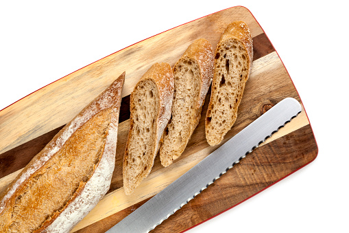 Sliced bread stick on board with knife.  Top view, over white.