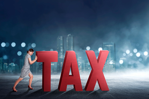 Beautiful asian business woman pushing away Tax text with cityscape background