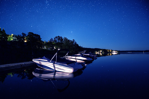 Boats float on the calm, still lake as thousands of stars sparkle in the sky above.