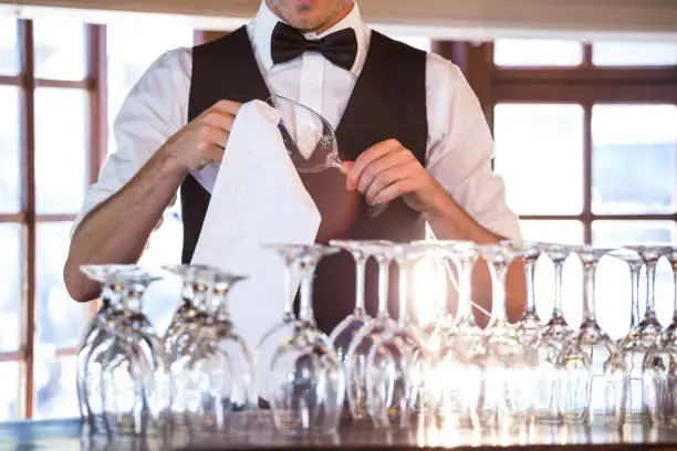 Mid section of bartender cleaning wine glass at bar counter