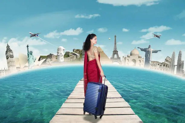 Back view of Indian woman walking on the dock while carrying a suitcase with famous landmark on the background