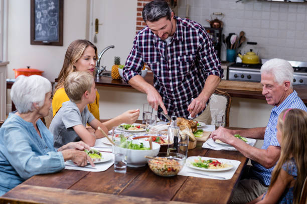 istock Man cutting roasted turkey while having meal with his family 661392352