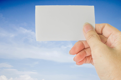 concept photo of right hand hold business card, credit card or blank paper on blurrd blue sky with white cloud
