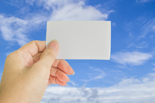 concept photo of left hand hold business card, credit card or blank paper on blurrd blue sky with white cloud