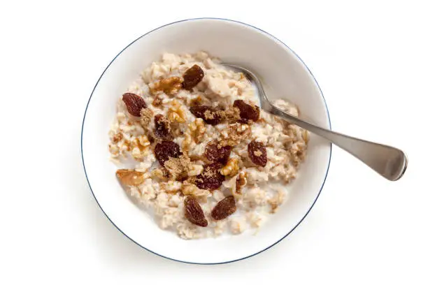 Bowl of oatmeal with raisins, walnuts and brown sugar.  Top view, isolated on white.
