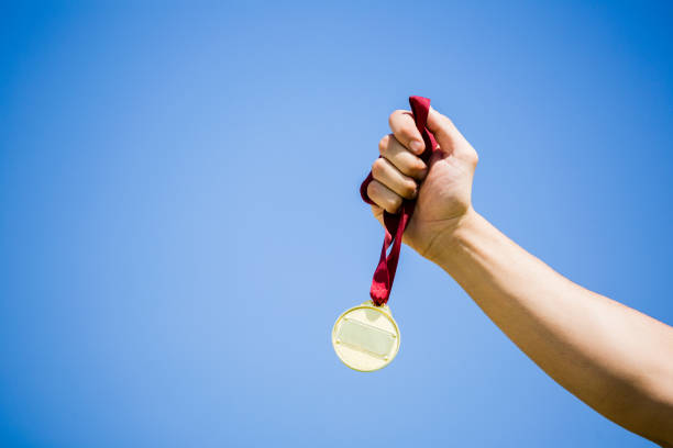 Close-up of athlete hand holding gold medal against sky