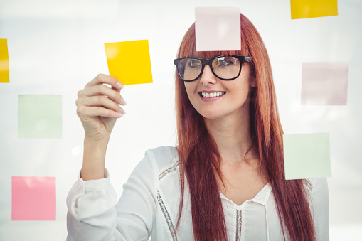 Attractive hipster woman looking at sticky notes in her office