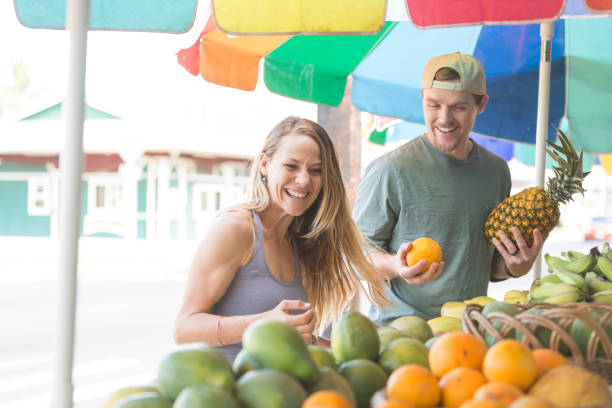 Aloha Life Young couple laughs and enjoys each other's company at fruit stand pitter stock pictures, royalty-free photos & images