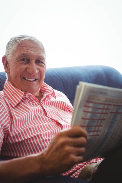istock Senior man seated on a sofa looking at camera while holding newspaper 661446990