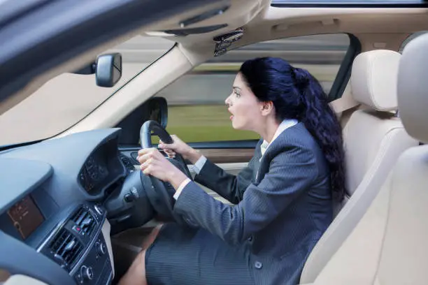 Picture of Indian businesswoman driving a car fast while wearing formal suit and looking at the road