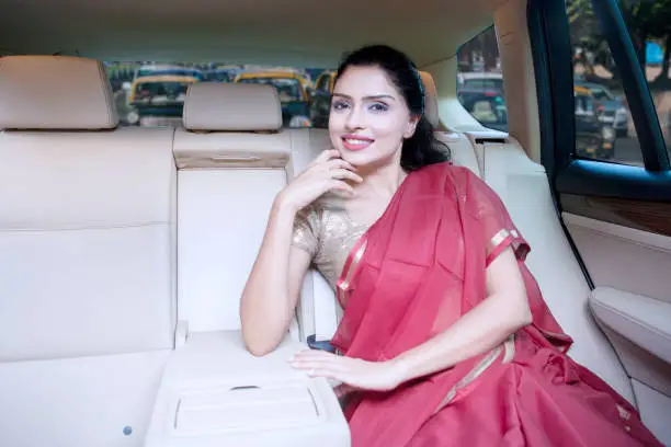 Portrait of a beautiful Indian woman smiling at the camera while sitting inside a car and wearing saree clothes