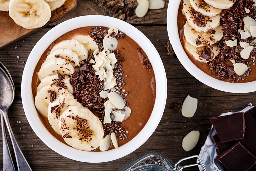 Chocolate smoothie bowl with banana, chia seeds and almond chips on wooden background